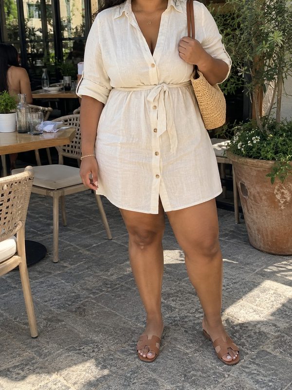 Example outfit cropped below the face: a cream belted linen shirt dress with tan slide sandals and a woven tote.