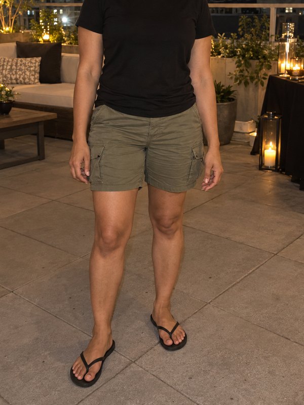 Example outfit cropped below the face: a black t-shirt, olive cargo shorts and black flip-flops on a rooftop at night.