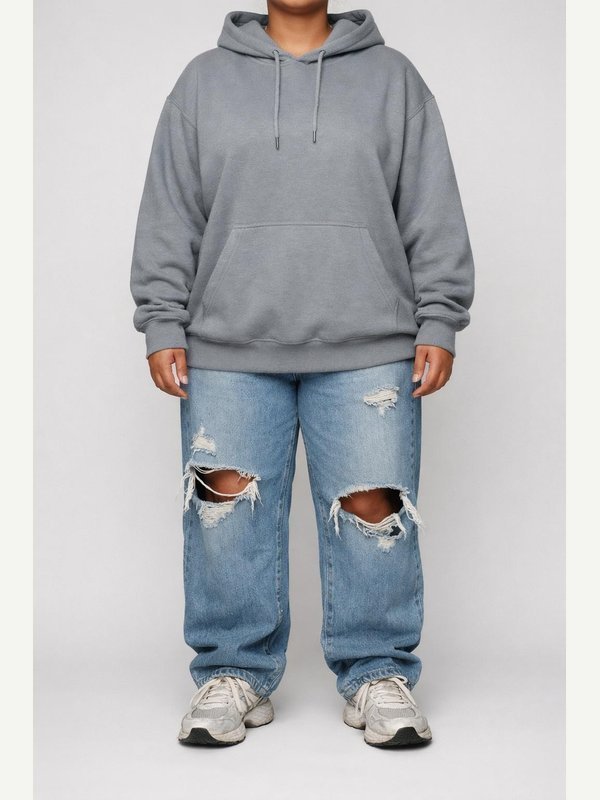 Adult woman in an oversized gray hoodie, baggy ripped blue jeans and worn white running sneakers.